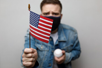 masked protesting young man holding an american flag. riots in america.