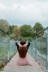 Girl sitting on the stairs in the park. Young woman in a pink skirt and black cheeks. Foreshortening from the back.