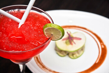 margarita de sandía y plato de ceviche de pescado con tapas de manzana verde y salsa picante sobre mesa de madera obscura, vista de cerca