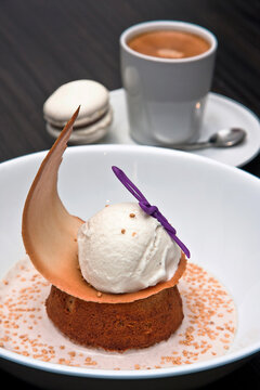 helado de coco sobre brownie y crema de coco, acompañado con taza de café y galleta, mesa de madera negra