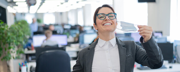 Business woman takes off the mask in the office at the end of quarantine. Coronavirus over time to...