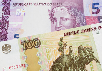 A macro image of a Russian one hundred ruble note paired up with a pink and purple five real bank note from Brazil.  Shot close up in macro.