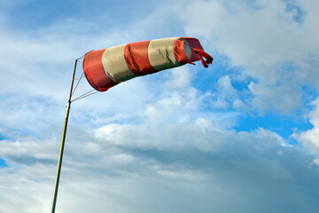 Meteorology wind bag for marine navigation. Red and white windsock blows against a blue sky