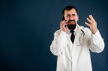 Male doctor with stethoscope in medical uniform displeased face and gestures and talking on cellphone