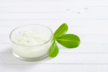 cosmetic cream in glass pot and leaves on white wood