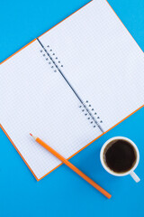 Open notepad and black coffee in the white cup on the blue  background. Location vetical. Copy space. Top view.