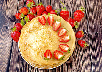 strawberries next to pancakes on a wooden table