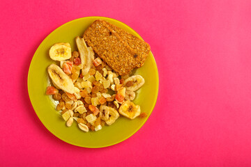 diet bread and granola on a green plate on a pink background.