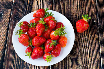 Ripe strawberries in the center of a white plate, on a wooden table