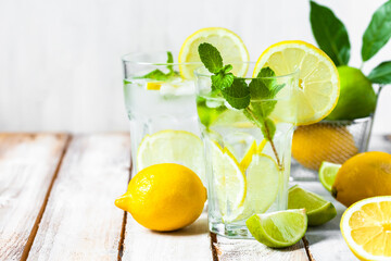 Concept of summer refreshing healthy alcohol free homemade lemonade with fresh pepper mint, limes and lemons. Low calories cold detox beverage. Wooden background, closeup. Copy space for text