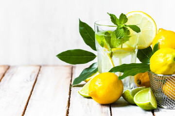 Concept of summer refreshing healthy alcohol free homemade lemonade with fresh pepper mint, limes and lemons. Low calories cold detox beverage. Wooden background, closeup. Copy space for text