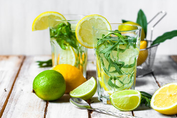 Concept of summer refreshing healthy alcohol free homemade lemonade with lemons, lime and tarragon. Low calories cold detox beverage. Wooden background, closeup