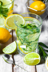 Concept of summer refreshing healthy alcohol free homemade lemonade with lemons, lime and tarragon. Low calories cold detox beverage. Wooden background, closeup