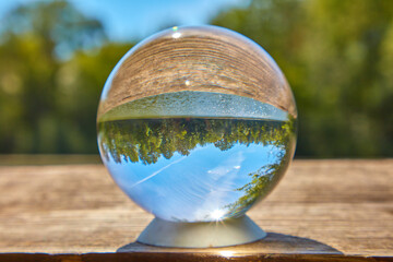 Eine Glaskugel liegt in der Sonne auf einem Steg an einem See.