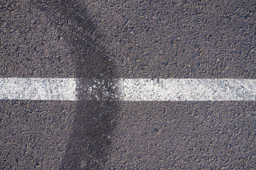 Fototapeta premium Asphalt texture with white line and tire marks. Smooth asphalt road. Tarmac dark grey grainy road background.Top view