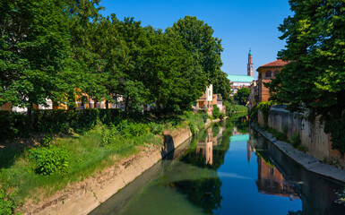 Fototapeta na wymiar The stretch of the Retrone river that crosses the city of Vicenza, runs along Piazza dei Signori, the Palladian Basilica and passes under the Ponte San Michele. Big trees, a clear spring day, Italy.