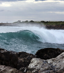 Side view of a beautiful clear wave that is just flipping and falling into the rest of the sea and crashed against cliffs and rocks. Detail on the sophistication of the sea level system. Paphos