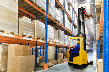 A large distribution warehouse with yellow forklift and orange, blue racks - obrazy, fototapety, plakaty