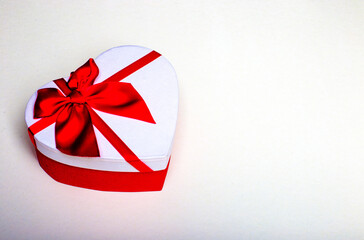 White gift in the form of a heart with a red bow on a white background close-up. Place to insert...