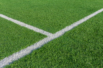 Green grass and white border lines on football ground. Soccer field on artificial turf. Artificial green grass texture. Artificial football field in an open stadium