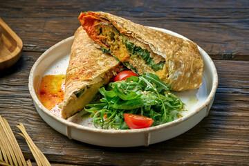 Vegetarian shawarma roll with spinach, tomatoes, hummus and melted cheese in a plate on a wooden background