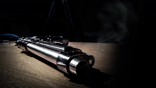 Cinemagraph of smoke emitted from the barrel of a silver 9mm pistol that lying on a wooden table. Close up, loop with selective focus.