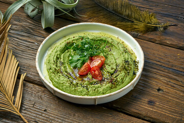 Classical oriental appetizer - avocado hummus with greens and cherry tomatoes in a white plate on a wooden background