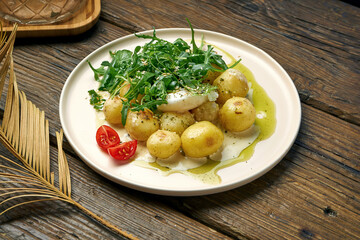 Boiled, young potatoes with arugula salad and poached egg seasoned with cream sauce on a wooden background