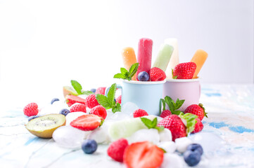 Healthy Whole Fruit Popsicles with Berries Kiwi strawberries on light background with a decor of ice, mint. Tasty fruit ice-cream in the mug. Copy space