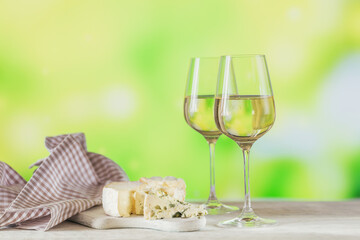 Two glasses of white wine served with cheese board on light green background. Wine mood concept