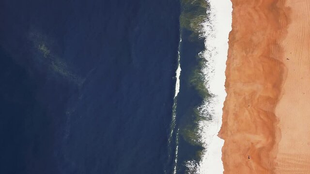 Flying over a sandy beach. Waves break on a sandy beach on the Atlantic coast, aerial View. Nazare, Portugal.