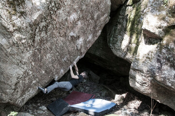 Rock climber under a big granite boulder. Outdoor bouldering. Extreme sport. Outdoor activity. Free climbing. Stone texture. Moss-coverd rock.