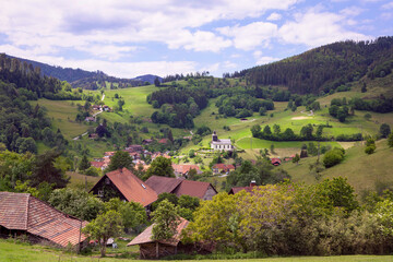 Fototapeta na wymiar Beautiful landscape with Schwarzwald mountains, village in the valley with church. Hills with green meadows and forest, blue sky. Black Forest panorama, Germany.