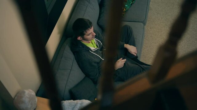 High quality close-up 4k slow motion video of a man sitting on a couch in his detached beautiful house main floor and watching television while browsing on the phone