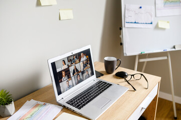 No people in office. An empty working place with a laptop on the desk, video call with a many people together on it