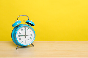 Blue vintage alarm clock at nine o’ clock on a yellow background with space for copy