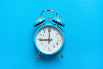 Blue vintage alarm clock at nine o’ clock lying on a blue background with space for copy seen from a high angle