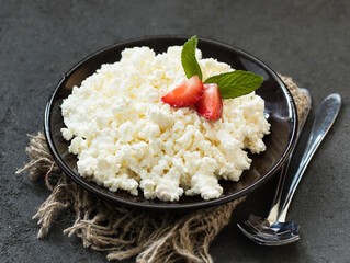 Cottage cheese with strawberries in a bowl on a linen napkin on a dark gray background
