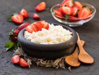 Cottage cheese with strawberries in a wooden bowl on a linen napkin in rustic style on a dark gray background