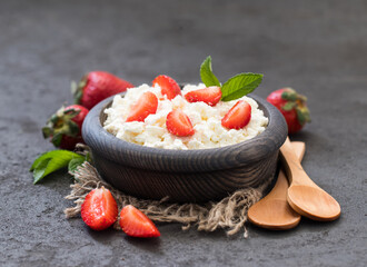 Cottage cheese natural with strawberries in a wooden bowl in rustic style on a dark background