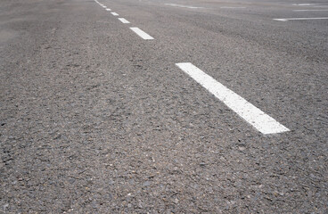 Dark asphalt road with marking lines. Tarmac texture. White disabled sign on a empty parking lot. Black tarmac texture with road marking 