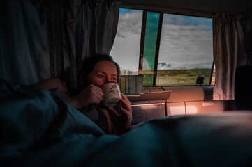 Woman enjoying coffee at the sunrise in the camper van on a roadtrip in Norway