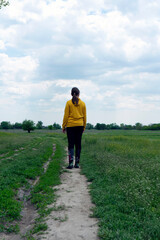 Girl in yellow walking on countryside path at early spring