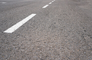 Dark asphalt road with marking lines. Tarmac texture. White disabled sign on a empty parking lot. Black tarmac texture with road marking 