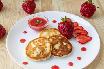 Three pancakes with cheese and strawberries and sauce on a white dish against wood background. Delicious cheese pancake and strawberries for the breakfast or lunch. Tasty meal with berries.