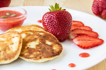 Three pancakes with cheese and strawberries and sauce on a white dish against wood background. Delicious cheese pancake and strawberries for the breakfast or lunch. Tasty meal with berries.