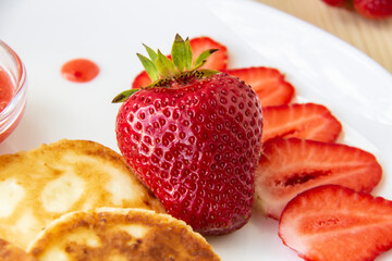 Pancakes with cheese and strawberries and sauce on a white dish against wood background. Delicious cheese pancake and strawberries for the breakfast or lunch. Tasty meal with berries.