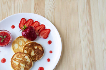 Three pancakes with cheese and strawberries and sauce on a white dish against wood background. Delicious cheese pancake and strawberries for the breakfast or lunch. Tasty meal with berries.