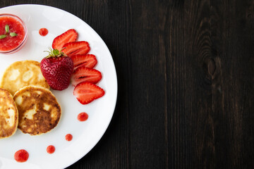Three pancakes with cheese and strawberries and sauce on a white dish against wood background. Delicious cheese pancake and strawberries for the breakfast or lunch. Tasty meal with berries.