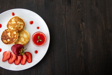 Fototapeta na wymiar Three pancakes with cheese and strawberries and sauce on a white dish against wood background. Delicious cheese pancake and strawberries for the breakfast or lunch. Tasty meal with berries.